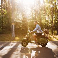 Picture of young bearded man on scooter outdoors. Looking aside.